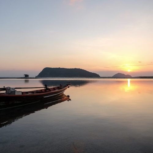 A boat on the sea surrounded by hills with the sun reflecting on the water during the sunset